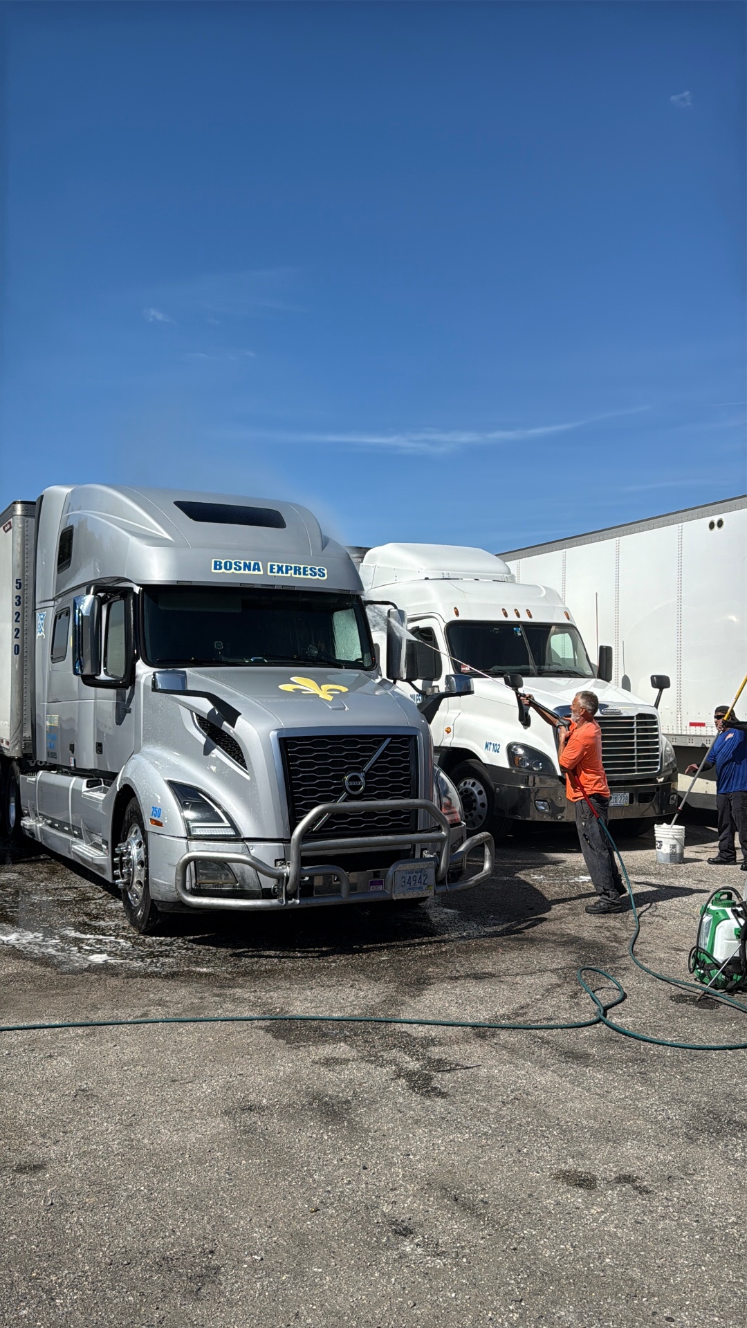 Sunset technician pressure washing a Volvo semi-truck on a commercial fleet route
